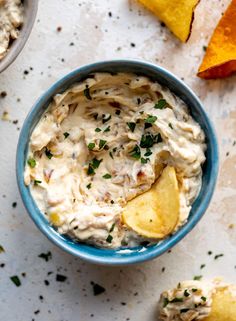 a blue bowl filled with potato chips and cream cheese dip next to an orange wedge