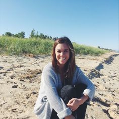 a woman is sitting on the beach with her hat in her hand and smiling at the camera