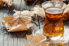 a glass cup filled with tea sitting on top of a wooden table covered in leaves