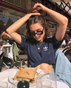 a woman sitting at a table with a sandwich in front of her and glasses on her head