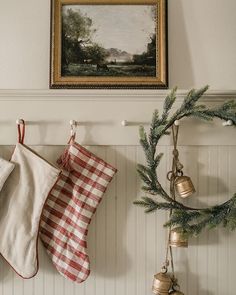 christmas stockings hanging on the wall next to a wreath and other holiday decorations in front of a painting