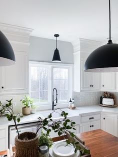 a kitchen with white cabinets and black pendant lights over the sink, potted plants on the counter