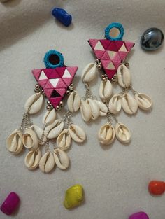 two pink and blue earrings with shells hanging from it's earwires next to candy