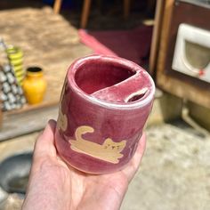 a hand holding a cup with a cat design on the outside and inside, in front of a table