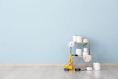 an empty room with blue walls and white paint rollers on the floor next to a shelf holding several rolls of toilet paper