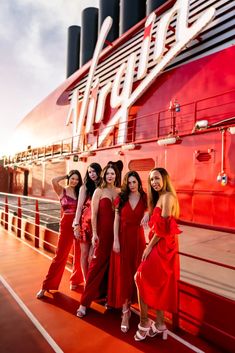 four women in red dresses standing on the side of a boat with their arms around each other