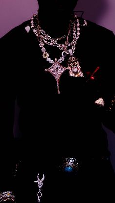 a man with many necklaces on his chest in the dark, wearing a black t - shirt