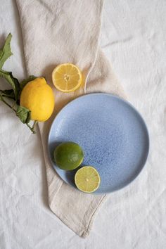 two lemons and one lime are sitting on a table cloth next to a blue plate