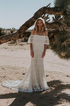 a woman standing in front of a tree wearing a white lace dress with off the shoulder sleeves