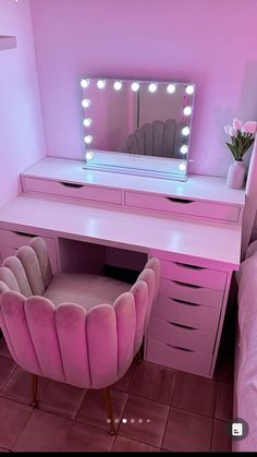 a pink vanity with lights on it and a chair in front of the mirror that is lit up