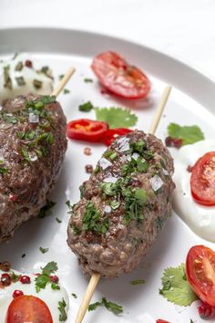 two meat skewers on a plate with tomatoes and eggs