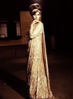 a woman wearing a gold dress and headpiece standing in front of a dark background