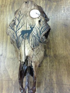 a deer skull with antlers and trees painted on it's face, sitting on a wooden table