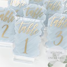 blue and gold wedding table numbers on acrylic paper with leaves in the background