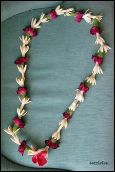 a necklace made out of flowers and leaves on a blue cushion with a red bow