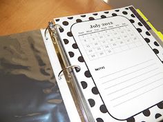 a black and white polka dot binder with a calendar on the front, next to a pen