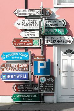 a bunch of street signs that are on the side of a pink building in front of a white door