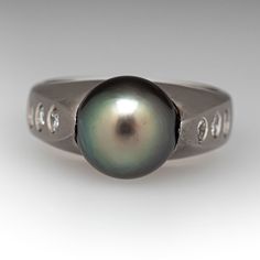 This exquisite ring is centered with one (1), post set, cultured Tahitian pearl. The top face of the shank are each accented with three (3), flush set, round brilliant cut diamonds. The ring measures 9.4mm at the top, rises 11.3mm above the finger, tapering to 4.2mm wide and 1.3mm thick at the base of the shank. This ring is currently a size 6.5 and shows some gentle wear to the satin finish. Classic Tahitian Pearl Ring For Anniversary, Elegant Pearl Ring With Bezel Setting For Formal Occasions, Elegant Pearl Ring With Bezel Setting For Formal Events, Classic Tahitian Pearl Ring For Formal Occasions, Elegant Formal Pearl Ring With Bezel Setting, Tahitian Pearl Rings With Diamond Accents For Anniversary, Formal White Gold Rings With Tahitian Pearl, Tahitian Pearl Ring With Diamond Accents For Wedding, Formal Tahitian Pearl Ring With Diamond Accents