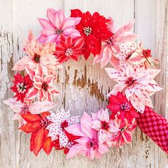 a wreath made out of red and pink poinsettis on a white wooden background