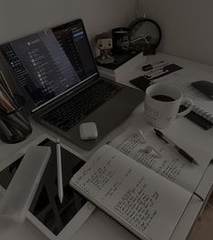 a laptop computer sitting on top of a desk next to a cup of coffee and notebook