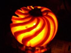 a lit candle in a glass container with an orange swirl on the top and bottom