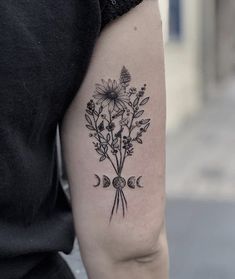 a black and white flower tattoo on the left upper arm, with crescent moon phases