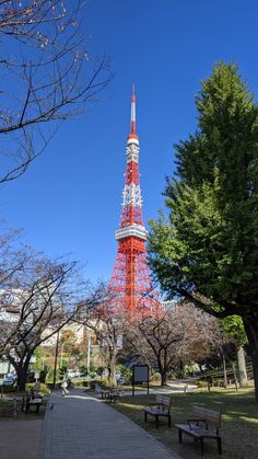 a red and white tower in the middle of a park with benches around it on a sunny day