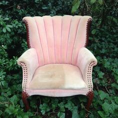 an old pink velvet chair sitting in the middle of some bushes and greenery,