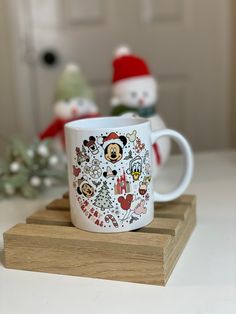 a mickey mouse coffee mug sitting on top of a wooden coaster next to a christmas tree