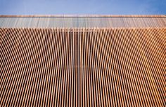 the side of a building that is made out of thin strips of wood, with a blue sky in the background