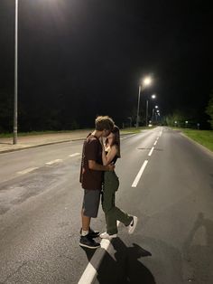 two people standing on the side of a road at night with their arms around each other