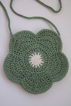 a green crocheted bag with a white flower on it's side and a string around the strap