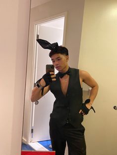 a man in a black outfit taking a selfie with his cell phone while wearing bunny ears