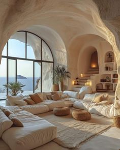 a living room filled with lots of white furniture and large windows next to a stone wall