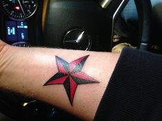 a red and black star tattoo on the left wrist by a steering wheel in a car