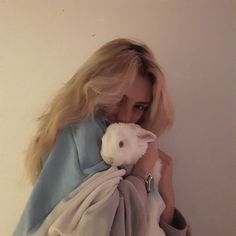 a woman holding a small white rabbit in her arms while wearing a blue and gray sweater