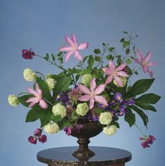 a vase filled with lots of flowers on top of a wooden table next to a blue wall