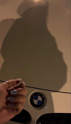 the shadow of a person holding a cell phone in front of a bmw emblem on a car