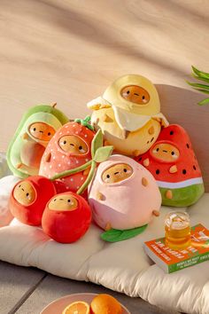 a pile of stuffed animals sitting on top of a pillow next to oranges and an apple