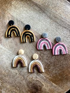 four pairs of earrings with rainbow design on wooden table next to black and white stones