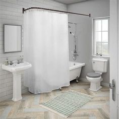 a white bathroom with herring tile flooring and shower curtain over the bathtub, toilet and sink