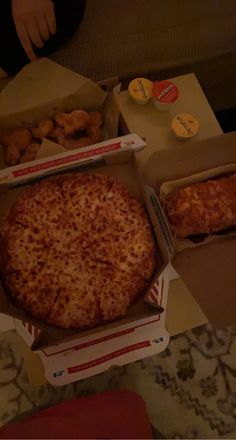 two pizzas in boxes sitting on top of a table next to some other food