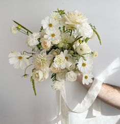 a bouquet of white flowers is held by a man's arm in front of a white wall