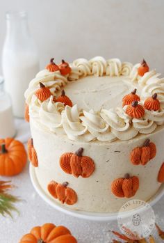 a white cake with orange frosting and pumpkins around it on a table next to milk bottles