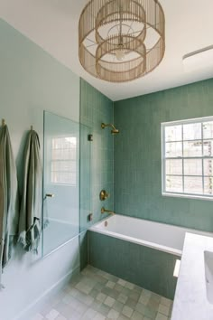 a bathroom with green tiles and a chandelier hanging from the ceiling over the bathtub