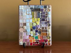 a multicolored mosaic tile with two black metal scissors on a wooden table in front of a brown wall