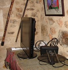 an old television and other electronics on a table in front of a stone wall with a painting