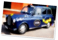 an old blue taxi with yellow flowers painted on it's side parked in front of a brick building