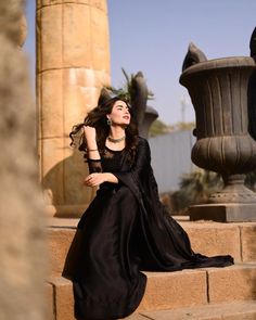 a woman is sitting on some steps wearing a black dress and heels with her hair blowing in the wind