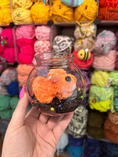 a hand holding a glass jar filled with crochet and yarns in it